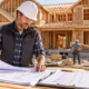 Residential builder reviewing house plans and a project estimate at a framed single-family home construction site.