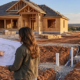 A homeowner and estimator review a house-building plan beside an Oklahoma home under construction, with site grading and drainage visible.