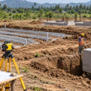 A site engineer surveys septic tank placement and drain-field layout before house construction as a contractor positions a precast tank.