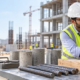 Engineer tests a concrete cylinder in a compression frame while comparing steel and timber samples to assess construction material strength.