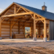 Post-frame pole barn construction with exposed timber supports, metal roof, open bay and builder reviewing plans.
