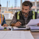 A construction accountant reconciles supplier invoices and tax records with the project manager in a commercial site office.