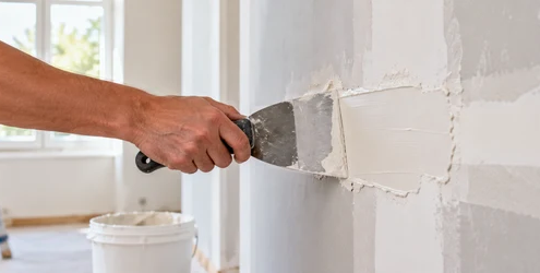Finisher spreads construction putty over a wall patch to create a smooth surface for finishing.