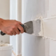 Finisher spreads construction putty over a wall patch to create a smooth surface for finishing.
