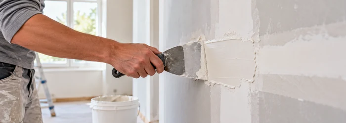 Finisher spreads construction putty over a wall patch to create a smooth surface for finishing.