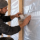 Builder tapes the vapor control layer seam against an insulated timber-framed wall.