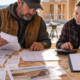 A contractor and bookkeeper calculate project overhead and profit from receipts, labor records, and a construction estimate.