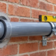 A plumber levels and secures a horizontal drain pipe through a sleeved opening in a brick wall.