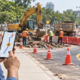 Commuter checking a roadwork map on a phone as crews and a detour close one lane