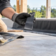Builder checks the tack of a thin rubber cement coat before bonding a rubber sheet