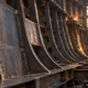 Inspector checks heavy steel plating and hull framing inside a ship under construction.