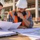 An accountant and construction manager review invoices, work orders, and project records at a commercial construction site to verify tax treatment.