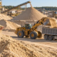 Engineer checks a sand sample at an active quarry as loaders and trucks transport construction sand.