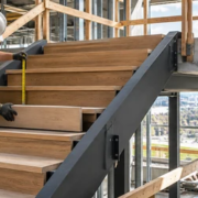 A stair carpenter measures the vertical rise between treads while an engineer checks the stair section and landing alignment.