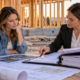 A homeowner and lender review documented borrower funds and a construction budget beside a framed house.