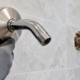 A plumber fits a brushed-nickel escutcheon around a shower arm to cover the tiled wall opening.