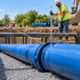 Workers check the bell-and-spigot joint of a coated ductile iron water main on trench bedding.