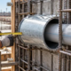 Worker checks a steel sleeve protecting a pipe opening through reinforced concrete before pouring.