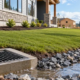 Graded home construction site with a storm drain inlet and stone swale directing water away from the foundation.