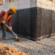 Workers place and compact backfill in a level lift around a protected building foundation