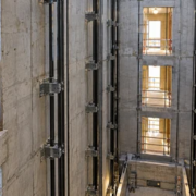 An engineer and elevator installer review guide rails and floor openings inside a protected concrete elevator shaft.