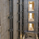 An engineer and elevator installer review guide rails and floor openings inside a protected concrete elevator shaft.
