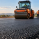 Road crew lays and compacts asphalt with a roller while an engineer checks the bituminous pavement surface.