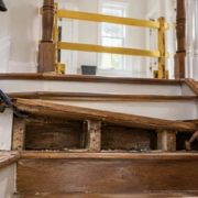 A carpenter carefully lifts a damaged stair tread to inspect the exposed stringer support while the stair is closed for repair.