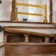 A carpenter carefully lifts a damaged stair tread to inspect the exposed stringer support while the stair is closed for repair.
