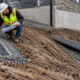 A civil engineer checks a surface-water interceptor drain that directs site runoff away from a building foundation to a catch basin.