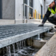 Construction worker inspects galvanized steel floor grating that lets water drain through its grid openings
