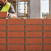 A mason builds a stack bond brick wall with uninterrupted vertical mortar joints while a supervisor checks course alignment.