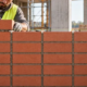 A mason builds a stack bond brick wall with uninterrupted vertical mortar joints while a supervisor checks course alignment.