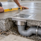 Stainless floor drain and outlet pipe installed flush within a concrete slab as an installer checks the finished surface.