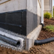 Gravel interceptor drain and perforated pipe carry water away from a house foundation toward a safe outlet.