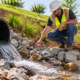 Drainage pipe daylighting at the surface into a stone-lined swale as a construction worker inspects the outlet.