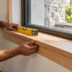 Carpenter fits and levels the interior window stool ledge at the base of a residential window