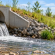 Stormwater outfall pipe discharging into a rock-lined channel while a civil engineer inspects erosion protection.