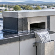 Roof scupper through a flat-roof parapet directing rainwater to a safe discharge while a roofer checks the flashing.