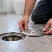 A plumber positions a removable floor cleanout cover beside the open drain access and cleaning cable.