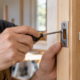 Carpenter aligns a metal striker plate on a wooden door jamb where the latch engages.