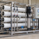 A water-treatment engineer checks gauges, controls and a treated-water sample beside a construction-site reverse osmosis system.