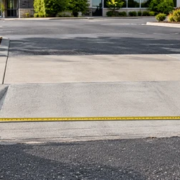Contractor measures the width of a concrete curb cut at a commercial driveway entrance to scope the work.