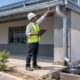 A site engineer checks a commercial roof gutter as a worker directs downspout runoff into a catch basin away from the foundation.