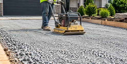Worker compacts a graded aggregate sub-base beneath a new residential driveway surface