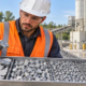 Materials engineer checks a graded tray of crushed stone ballast beside a concrete batching plant.