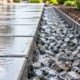 Worker checks a contained gravel edge beside a paved path to help prevent washout and improve drainage.
