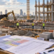 A construction cost engineer checks a work-package cost matrix alongside site plans, material samples, and active commercial building work.