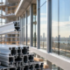 Worker examines aluminum extrusion profiles beside glazed facade framing under construction.