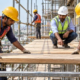 Workers fit supported timber planks across a scaffold to create a level construction work platform